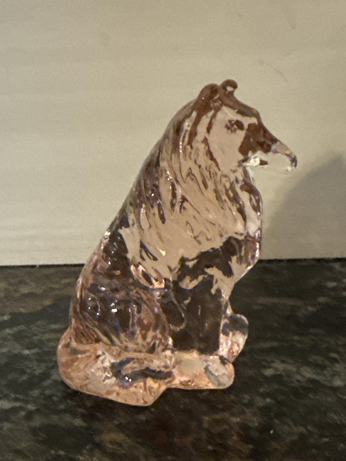 Side view of pink glass collie statue on a dark surface.