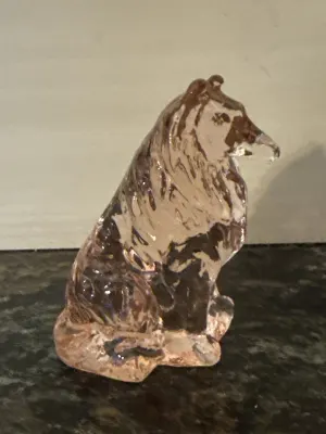 Side view of pink glass collie statue on a dark surface.
