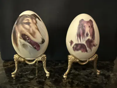 Two painted eggs with collie images on gold stands.