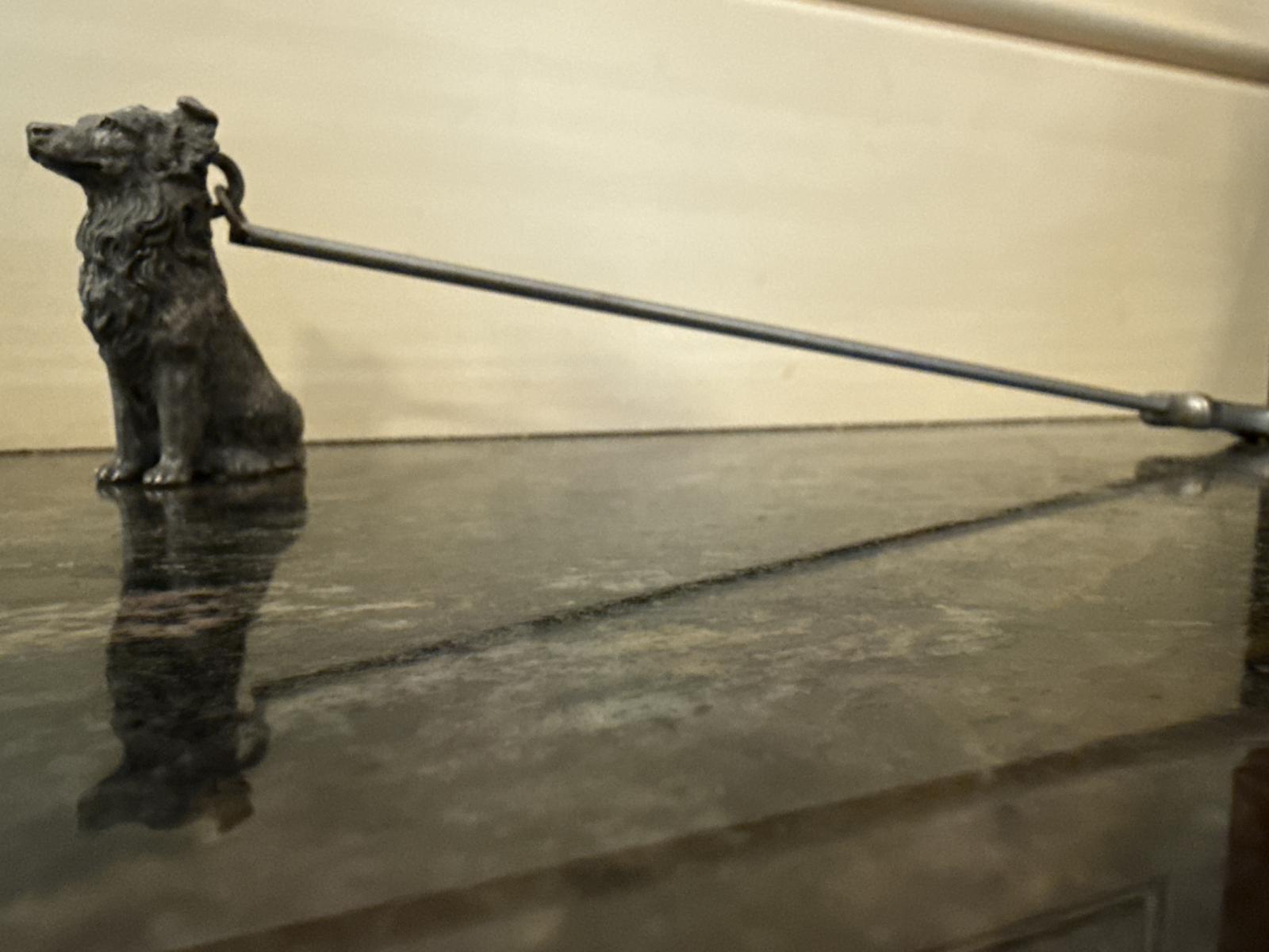 Side view of metal collie candle snuffer on a surface.