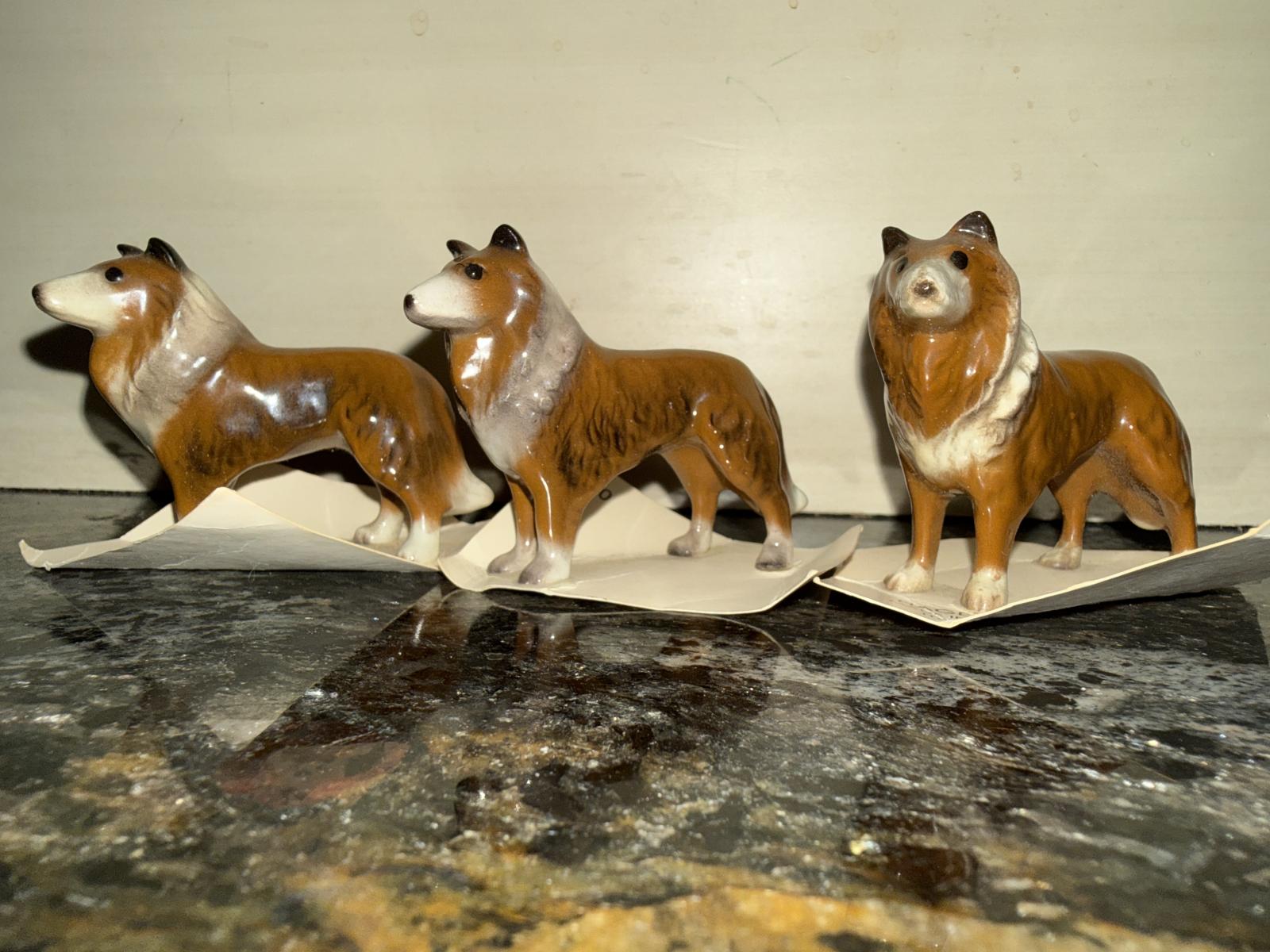 Three miniature collie figurines on a surface, side by side.
