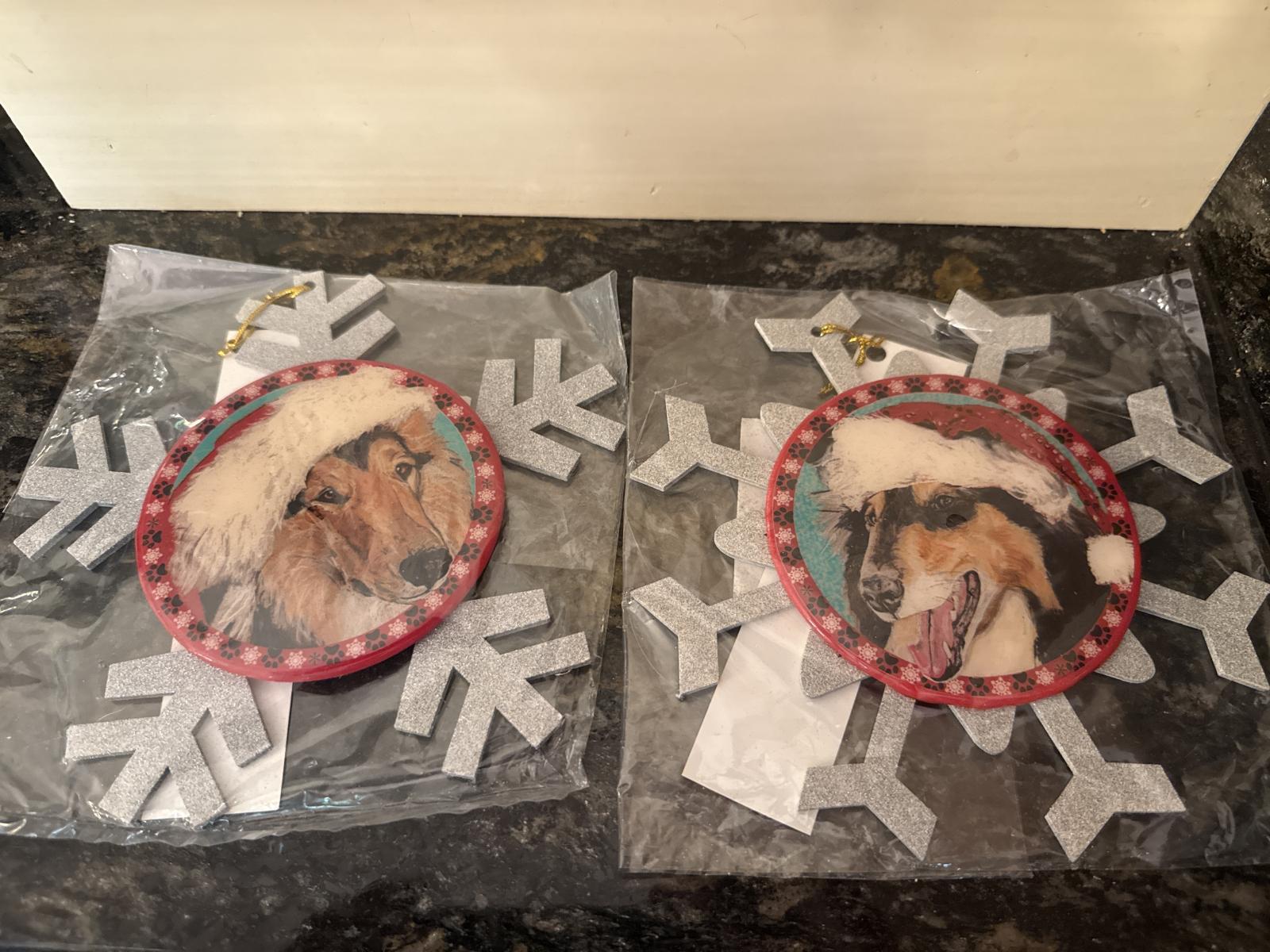 Two collie Christmas ornaments with snowflake design and Santa hats, in packaging.