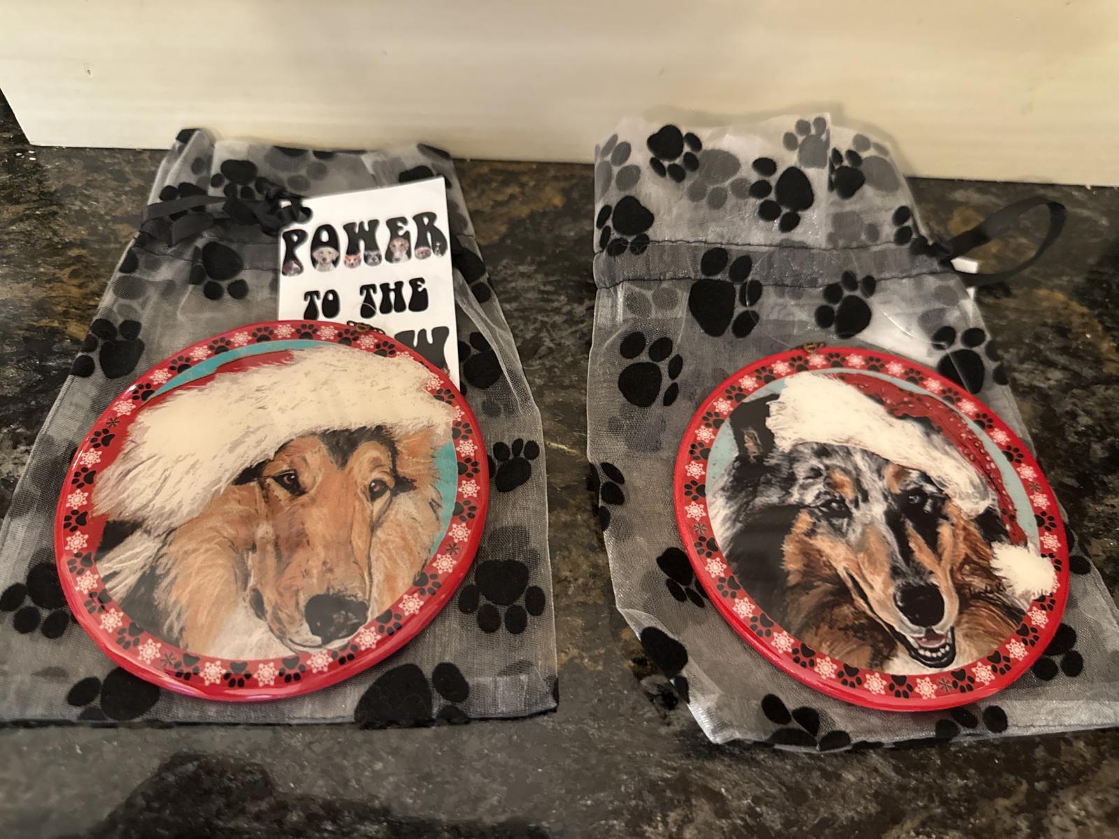 Two collie Christmas ornaments with Santa hats on paw print bags.