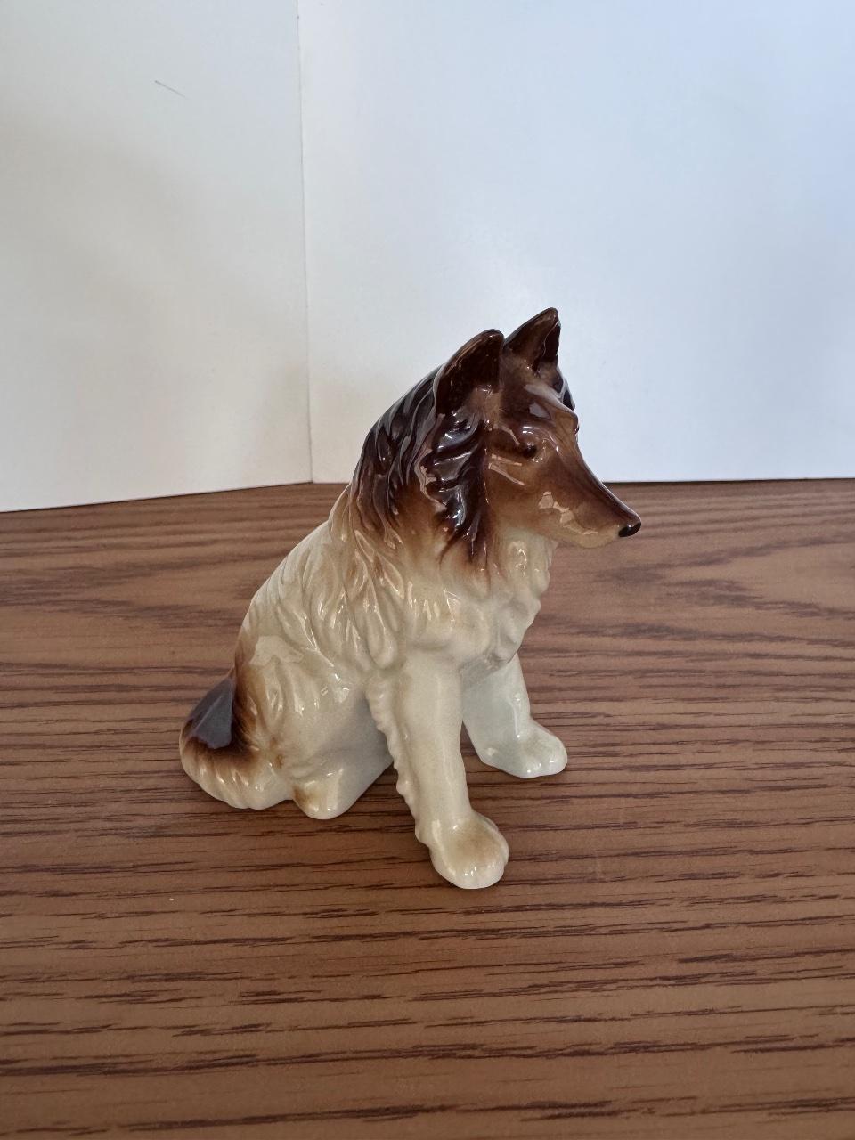 Ceramic collie figurine with brown and white glaze on a wooden surface.