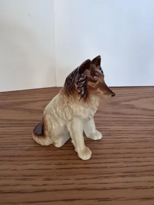 Ceramic collie figurine with brown and white glaze on a wooden surface.