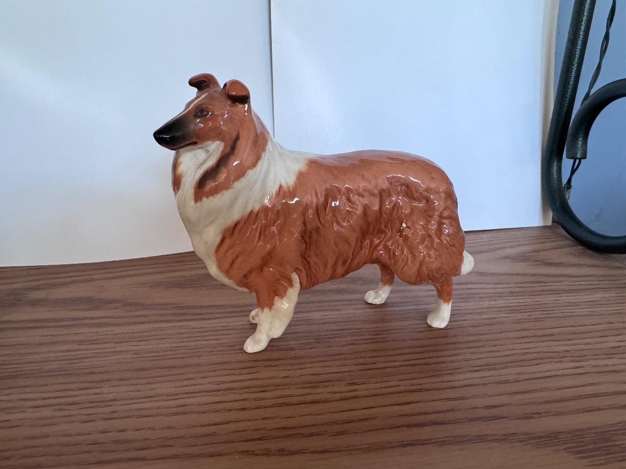 Ceramic collie statue with brown and white colors on a wooden surface.